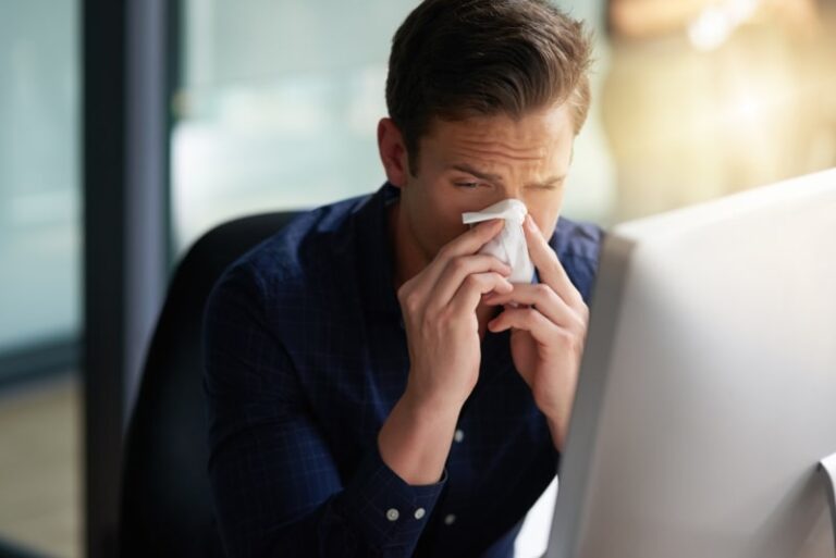 man blowing nose in front of computer min