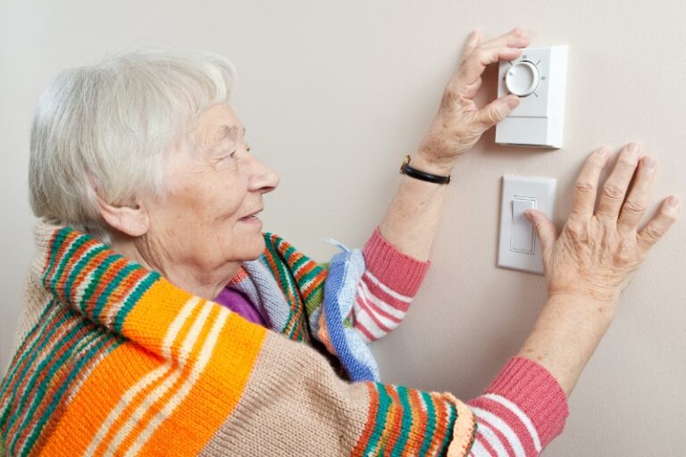 senior woman adjusting thermostat min