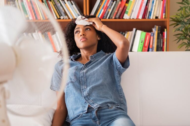 unhappy woman dabbing her sweat in front of fan